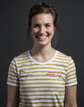 Portraitbild von Caroline Flegel, Unified Partnerin im Kanu. Ihre dunklen Haare sind zurückgesteckt. Sie lacht herzlich in die Kamera und trägt ein horizontal weiß gelb gestreiftes T-Shirt.