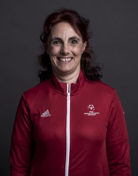 Portraitfoto von Andrea Mönch, Nationale Koordinatorin Badminton. Sie trägt offene lockige lange Haare und eine rote Trainingsjacke mit dem Special Olympics Deutschland Logo. Sie lacht herzlich in die Kamera.