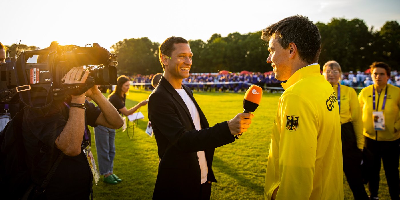 Ein ZDF Reporter mit Kameramann interviewt einen Team SOD Athleten bei der Eröffnungsfeier der Weltspiele Berlin 2023